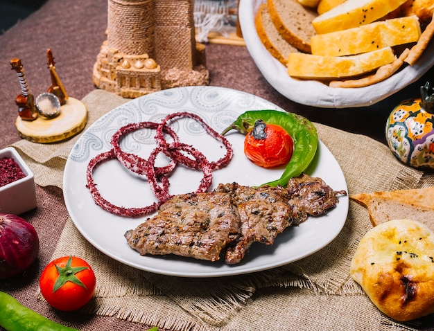 Front view meat basturma kebab with tomato and hot pepper on the grill with onion in sumac