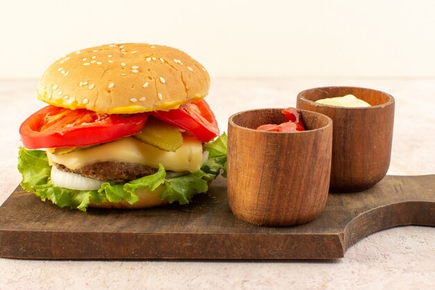 A front view meat burger with cheese and green salad along with ketchup and mustard on the wooden table 