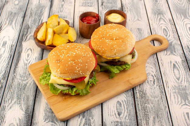A front view meat burger with cheese and green salad potatoes and dips on the wooden table and grey table