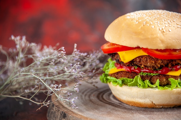 Бесплатное фото Вид спереди мясной бургер с сырными помидорами и салатом на темном фоне