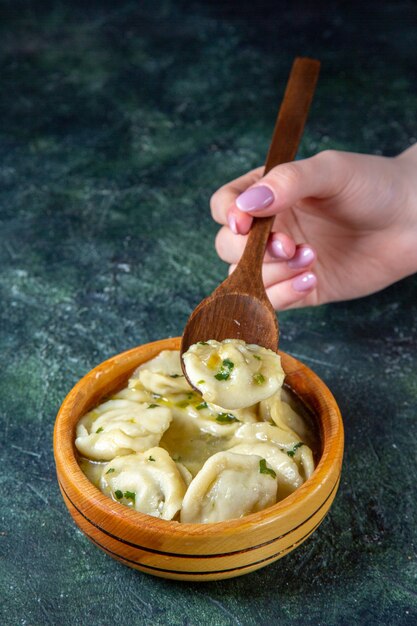 Front view meat dumplings with female putting wooden spoon into it on dark surface