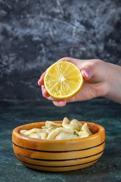 Front view meat dumplings with female squeezing lemon into it on dark surface