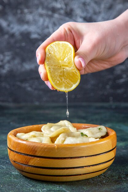 Front view meat dumplings with lemon juice squeezing by female on dark blue surface