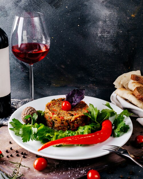 正面の肉料理と新鮮な野菜、茶色の机と灰色の表面に赤ワイン