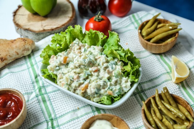 Столичный салат вид спереди с кетчупом и майонезом, помидорами и перцем на столе