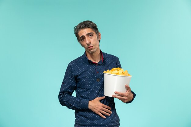 Front view middle-aged male eating cips on blue surface