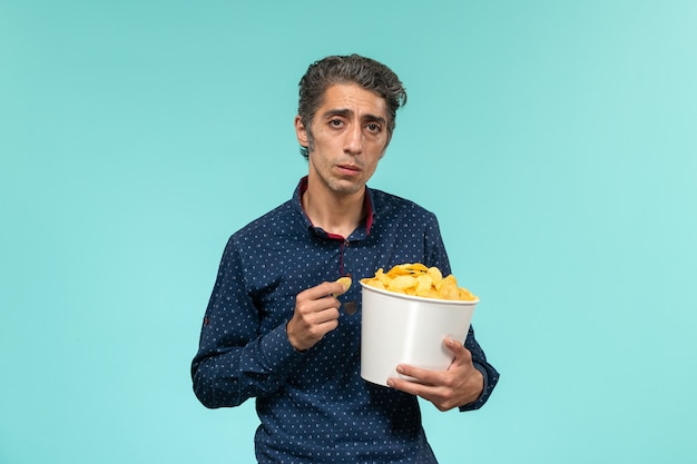 Мужчина средних лет, вид спереди, ест чипсы на синей поверхности
