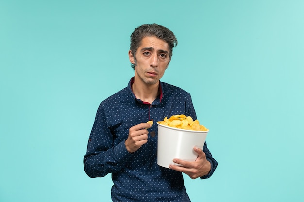 Front view middle-aged male eating cips on the blue surface