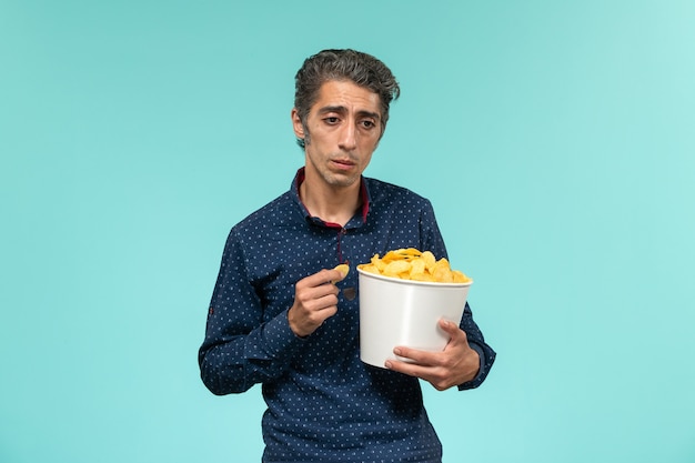 Мужчина средних лет, вид спереди, ест чипсы и подчеркивает синюю поверхность