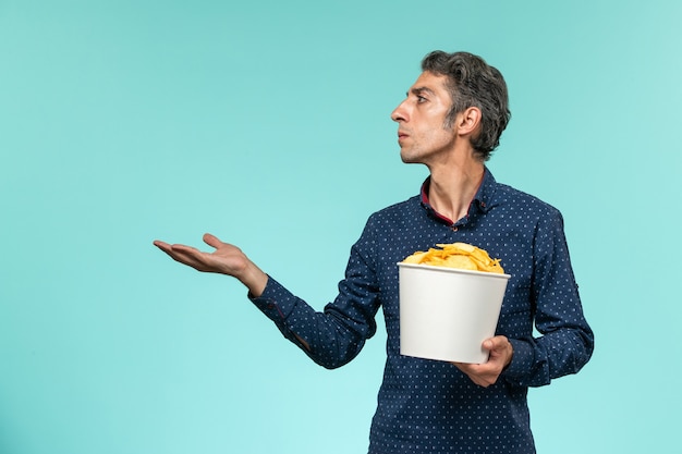 Front view middle-aged male holding basket with potato cips on blue desk