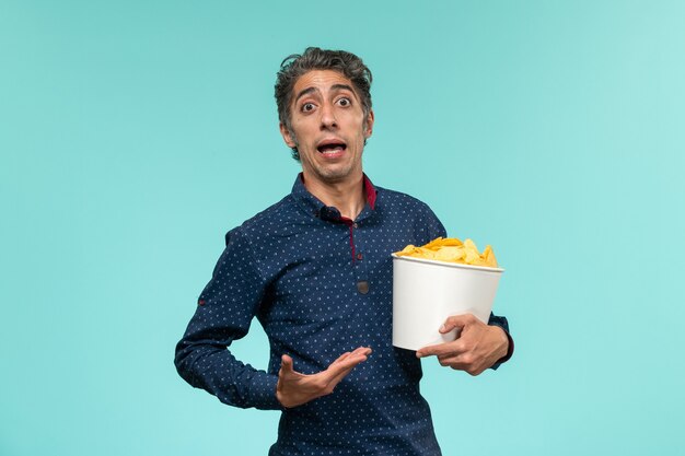 Front view middle-aged male holding basket with potato cips on blue surface