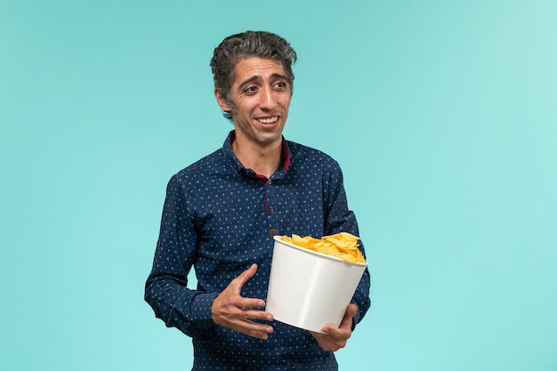 Front view middle-aged male holding basket with potato cips on light-blue surface