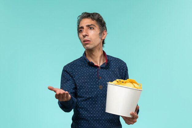 Front view middle-aged male holding basket with potato cips on light-blue surface