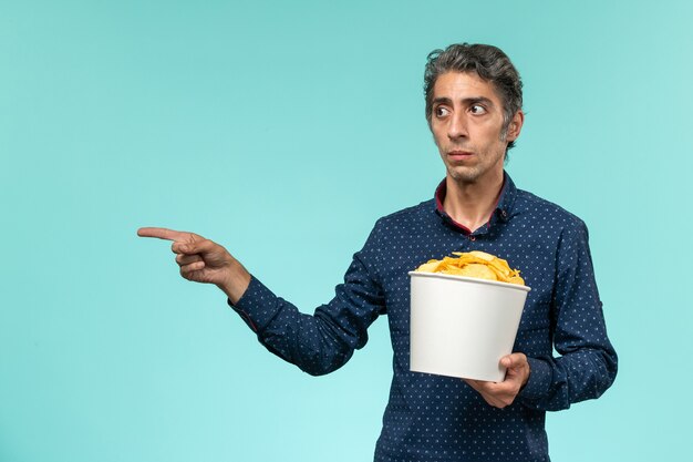 Front view middle-aged male holding basket with potato cips on light blue surface