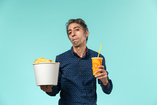 Front view middle-aged male holding potato cips and soda on a blue surface