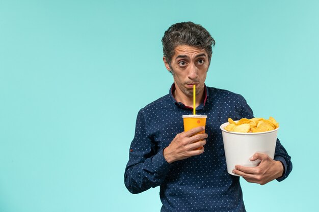 Front view middle-aged male holding potato cips and soda on a light blue surface