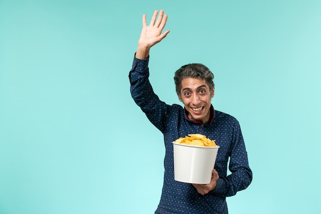 Front view middle-aged male holding potato cips and waving on a blue surface