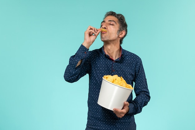 Front view middle-aged male with basket full of cips and eating on the blue surface