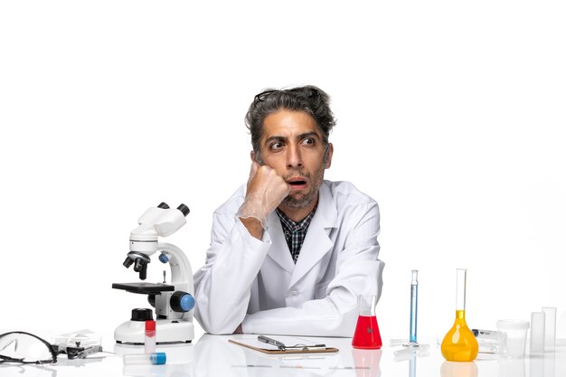 Front view middle-aged scientist in medical suit sitting around table with solutions