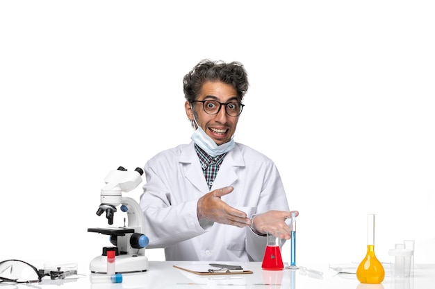 Front view middle-aged scientist in special suit sitting around table with solutions