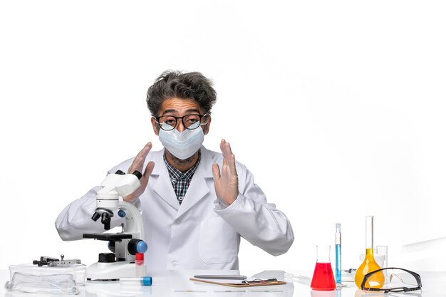 Front view middle-aged scientist in special suit sitting around table with solutions