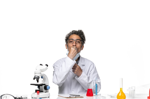 Front view middle-aged scientist in special suit sitting around table with solutions