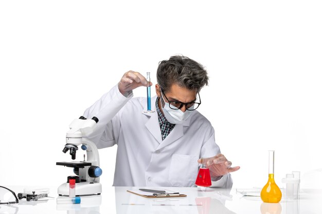 Front view middle-aged scientist in special suit sitting and holding flasks with solutions