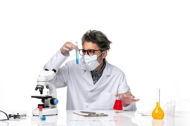 Front view middle-aged scientist in special suit sitting holding flasks with solutions