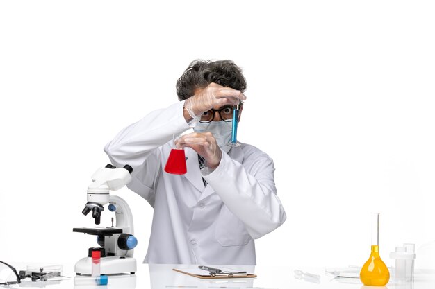 Front view middle-aged scientist in special suit sitting holding flasks with solutions