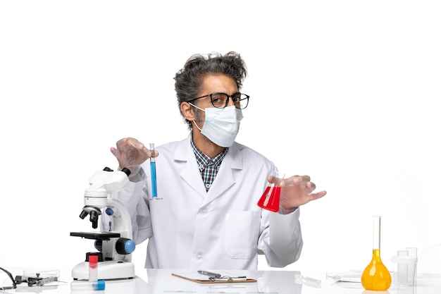 Front view middle-aged scientist in special suit sitting holding flasks with solutions