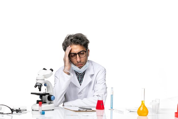 Front view middle-aged scientist in special white suit sitting around table with solutions