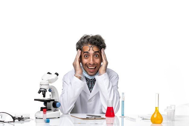 Front view middle-aged scientist in special white suit sitting around table with solutions