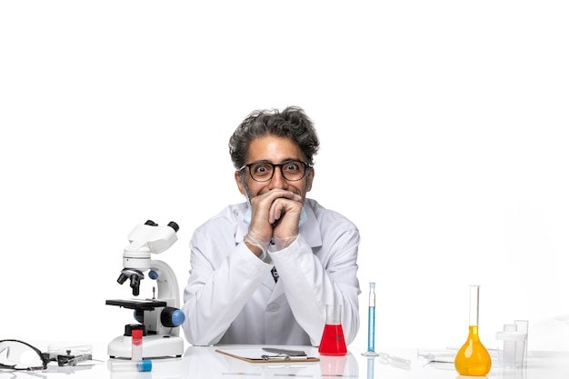 Front view middle-aged scientist in special white suit sitting around table with solutions