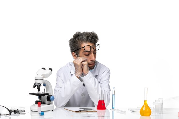 Front view middle-aged scientist in special white suit sitting around table with solutions