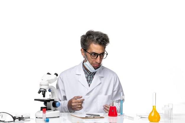 Front view middle-aged scientist in special white suit sitting around table with solutions