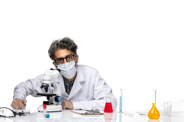 Front view middle-aged scientist in special white suit using microscope