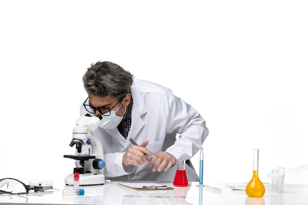 Front view middle-aged scientist in special white suit using microscope