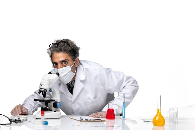 Front view middle-aged scientist in special white suit using microscope