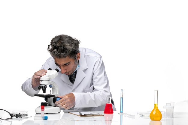 Front view middle-aged scientist in special white suit using microscope