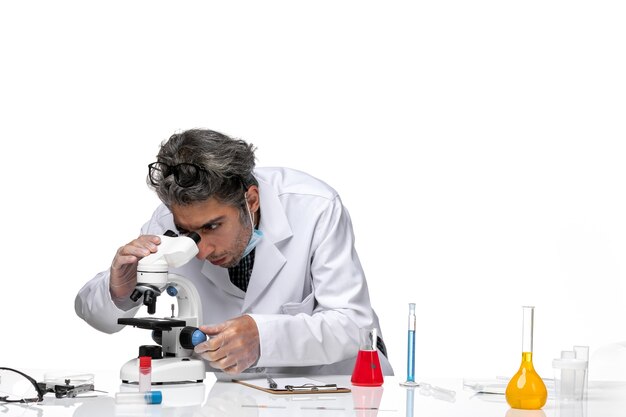 Front view middle-aged scientist in special white suit using microscope