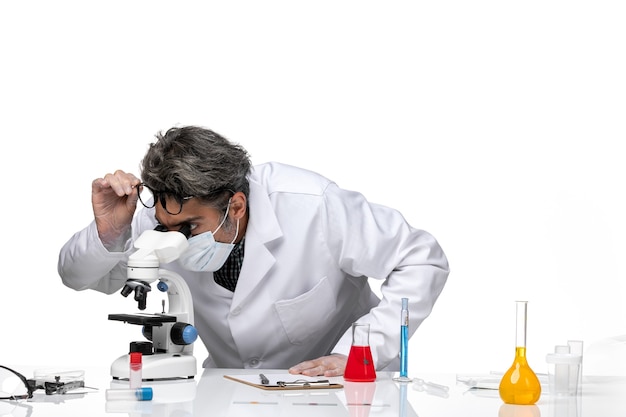 Front view middle-aged scientist in special white suit using microscope