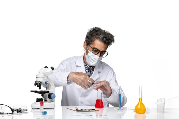 Front view middle-aged scientist in white medical suit filling injection with red solution