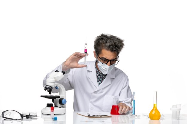 Front view middle-aged scientist in white medical suit filling injection with red solution