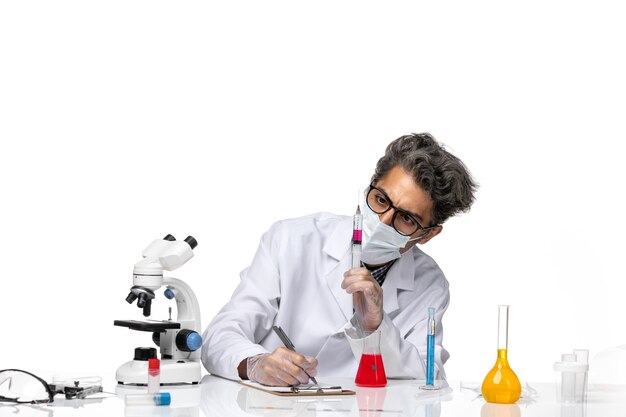 Вид спереди ученого средних лет в белом медицинском костюме, заполняющего инъекцию красным раствором