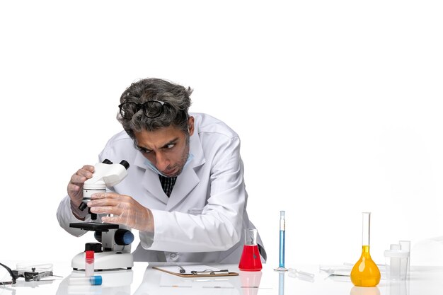 Вид спереди ученого средних лет в белом медицинском костюме, фиксирующего микроскоп