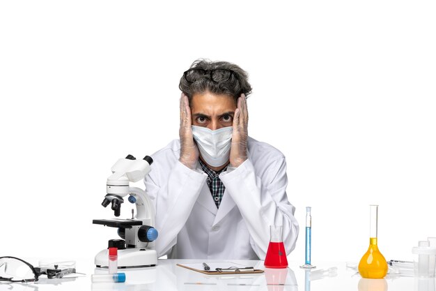 Front view middle-aged scientist in white medical suit sitting around table with solutions