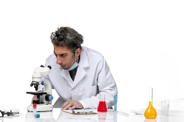 Front view middle-aged scientist in white medical suit using microscope