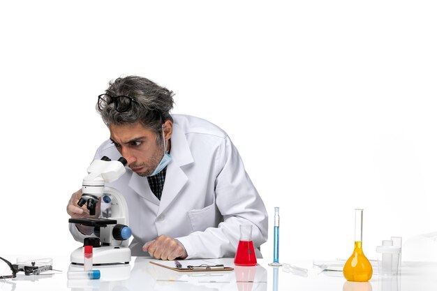 Вид спереди ученого средних лет в белом медицинском костюме с помощью микроскопа
