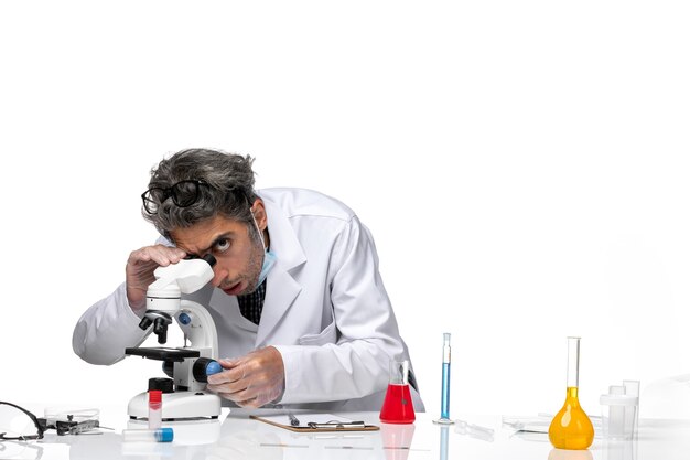 顕微鏡を使用して白い医療スーツを着た中年の科学者の正面図