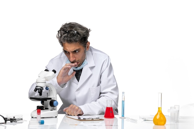 Front view middle-aged scientist in white medical suit using microscope